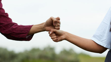 Two people fist bumping with a blurred natural background